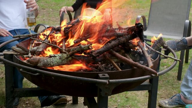 People relaxing at backyard fire pit with burning logs