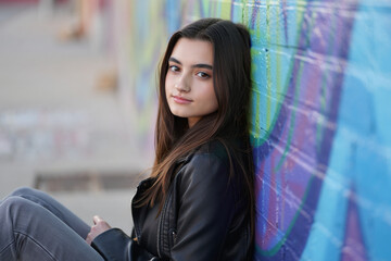 Obraz premium Teenage girl leaning against colorful graffiti wall wearing black leather jacket