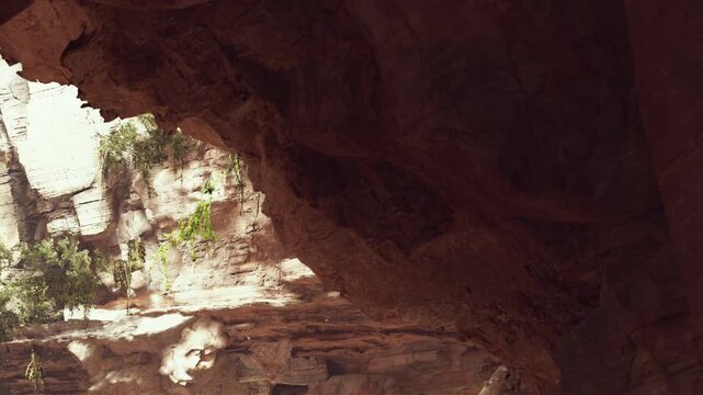 Visitors explore a canyon with large rock formations and greenery. The sunlight shines down, creating shadows on the canyon walls. It is daytime and the scene shows natural beauty.