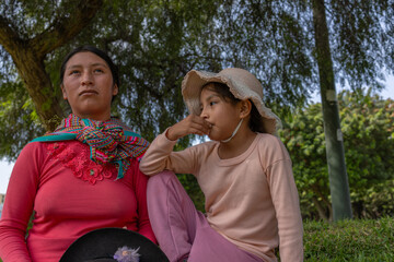 Fototapeta premium Authentic low angle portrait of an indigenous mother and daughter seated outdoors, expressing contemplation, connection and cultural identity.