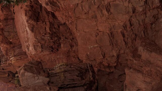 The scene shows rocks and stones inside a cave. The cave walls are red and rough. Sunlight shines into the cave, highlighting the texture of the rocks.