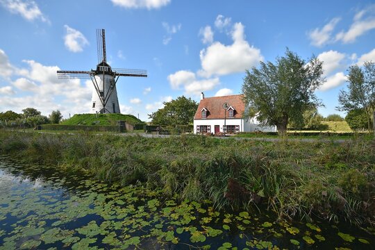Landscape with scenic view of a typical Flemish rural house and the historic windmill of Schellemolen on the banks of Damse Vaart in Damme, West Flanders Belgium.