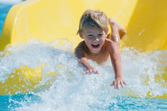 Child mid-air splashing down a bright yellow water slide into a pool, with water droplets and waves visible around the excited young boy
