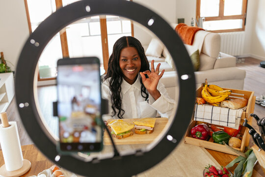 Black woman influencer creating video content for recipe with sandwiches, using a ring light