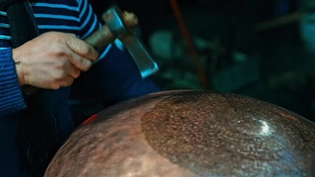 Close up shot of a coppersmith master working on copper plate in slow motion. Focus on hands, hammer and authentic details of traditional craft.