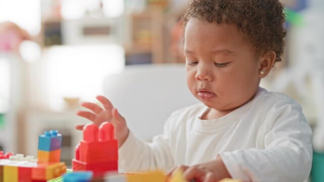 Little girl stacks colorful plastic blocks with hand reaching and precise grasp on a tabletop in a bright play area inside a building; play learning concentration.