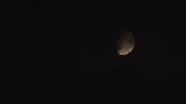 Moon transit across a night sky with clouds obscuring