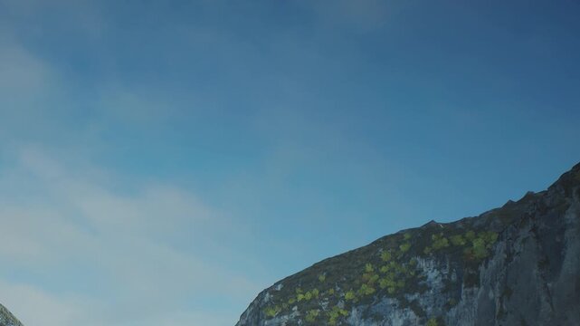 The sun rises above the mountain peaks as the sky turns lighter. A few clouds float gently in the clear blue sky. Green patches are visible on the rocky slopes.