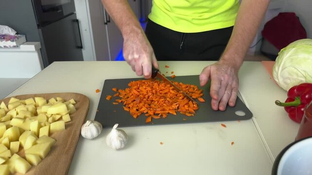 Midsequence homecook chopping carrots on cutting board during meal preparation with surrounding
