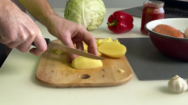 Hands slicing peeled potato into wedges on wooden cutting board midsequence kitchen prep scene