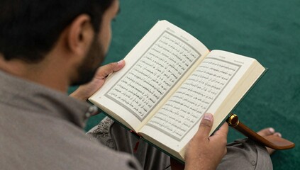 Naklejka premium Man attentively reading from the Quran in arabic script with traditional wooden book holder