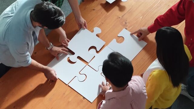 Top view of skilled business people gathering jigsaw piece together.Startup team with casual cloth standing at table while put jigsaw on table. Show unity, cooperation and team working. Convocation.