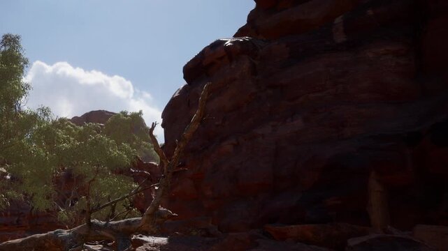 In a dry landscape, a person is climbing rocky terrain under a clear blue sky. Green trees are visible nearby, and clouds are partly covering the sun.