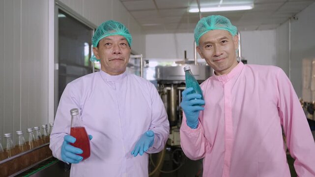 Professional Asian technician and inspector in uniform of food and drink factory holding a juice beverage bottle promoting healthy nutritional benefits in production line at manufacturing industry. 