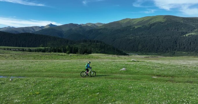 Aerial footage of woman riding mountain bike on beautiful grassland mountain trail, slow motion
