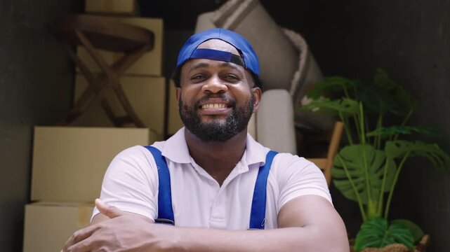 Happy professional African man mover service and delivery in a company uniform and cap standing smiling with arms crossed while looking at the camera with relaxing after finishing loading onto truck.