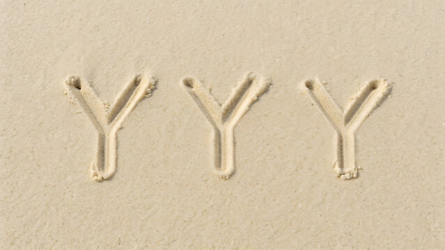 Three uppercase letter y characters written in the fine beige sand of a beach, view of handwritten alphabet letters on a sandy surface