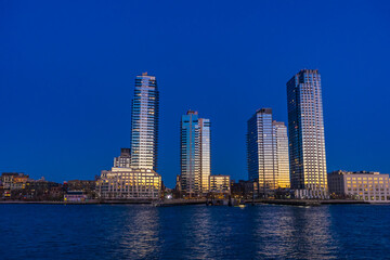 Obraz premium Modern waterfront skyline with illuminated residential skyscrapers at blue hour