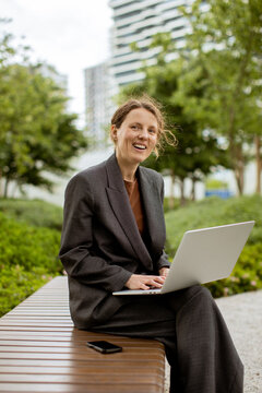Woman works on laptop in outdoor park setting during sunny day in urban area