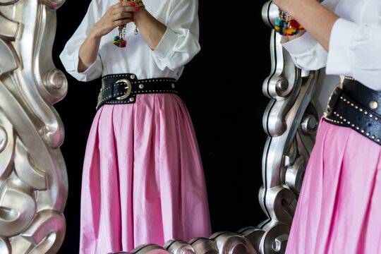 Mid section of a woman wearing a stylish black belt with golden buckle, holding a colorful beaded accessory while posing in front of a large ornate silver mirror.