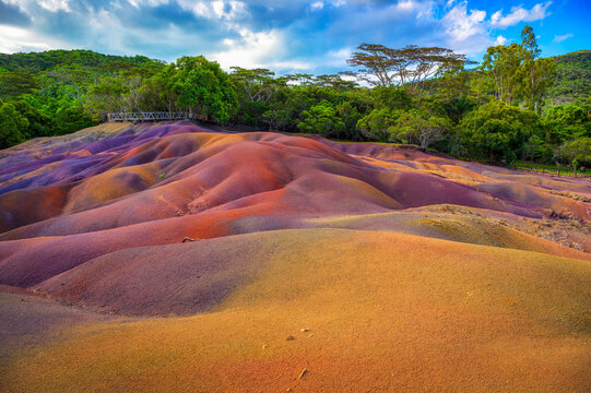 Chamarel, Riviere Noire, Mauritius - February 20, 2025 : Rippled, multicolored dunes of the Seven Colored Earth Geopark with lush rainforest backdrop under dramatic clouds.