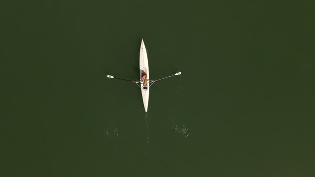 Aerial view of a person rowing a white scull boat on dark green water with ripples from the oars in Nevers, Bourgogne-Franche-Com, France.