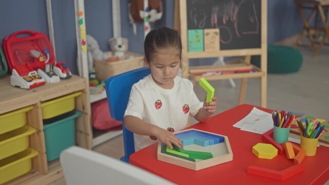 Girl placing green wooden blocks into a hexagon puzzle on a red table in a classroom; concentration learning play.