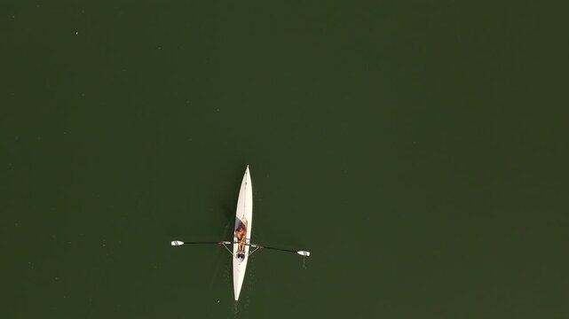 Aerial view of a person rowing a white scull boat on the calm dark green surface of a river in Nevers, Bourgogne-Franche-Comte, France.