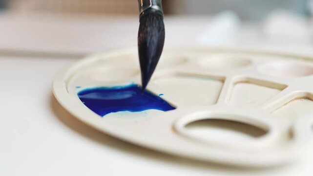 Closeup of artist hand mixing vibrant blue watercolor paint on palette