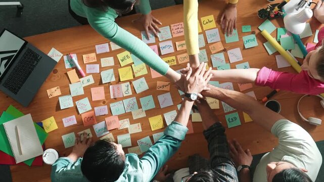 Top down view of designer standing at meeting with sticky note and putting hand together. Aerial view of team make stack of hand to celebrate successful project or after brainstorming idea. Symposium.