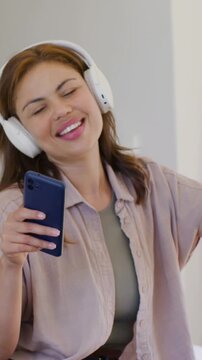 Vertical video: Song starting, woman in top singing, swaying in bedroom with phone and headset