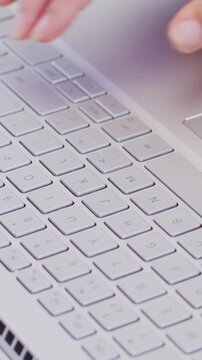 Vertical video: Tapping trackpad, hands typing keys on silver laptop at desk for work, dark sleeve