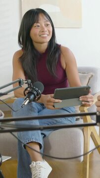 Vertical video: Replying to cue host in maroon top holding tablet speaking into mic in home studio