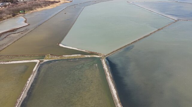 Aerial view of the colorful salt evaporation ponds at Lake Atanasovsko with narrow dikes and calm water in Burgas, Bulgaria.