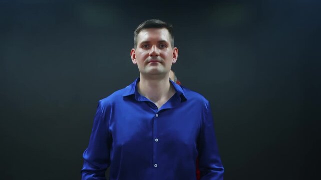 Adult man wearing bright blue collared shirt stands with composed posture against dark teal backdrop, displaying calm confidence, suitable for professional, corporate, or portrait concepts.