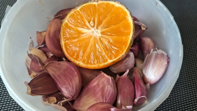 Half of a fresh orange resting atop raw purple garlic cloves