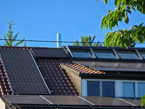 older house roof partially covered with pv modules beside fresh green branches beneath clear blue sky