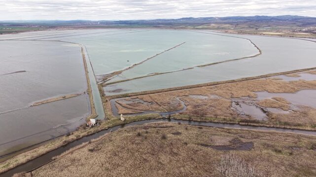 Aerial view of Lake Atanasovsko salt pans with dikes, canals, and a small building under a cloudy sky in Burgas, Bulgaria.