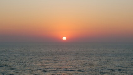 Obraz premium Sunset over calm ocean waters with orange sky