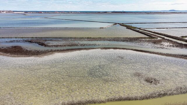 Aerial view of Lake Atanasovsko salt pans showing the geometric patterns of the water basins and narrow dikes under a clear sky in Burgas, Bulgaria.
