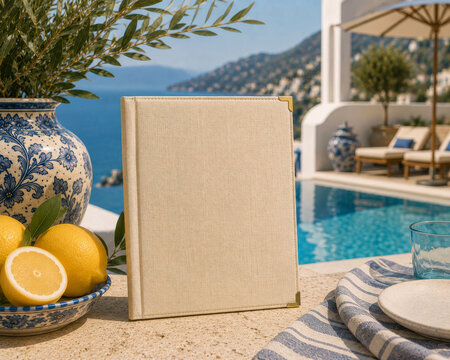 A luxury Mediterranean menu mockup displayed beside a resort pool with lemons, ceramic decor, and coastal scenery, featuring a blank linen-covered menu cover for premium branding.
