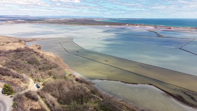 Aerial view of Lake Atanasovsko showing the segmented salt evaporation ponds and coastal landscape under a bright sky in Burgas, Bulgaria.