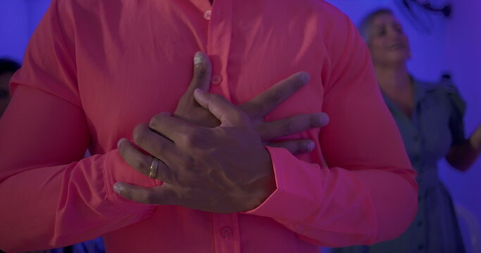 Man in bright shirt sings with hands crossed over chest during church gathering, surrounded by congregation in peaceful spiritual moment