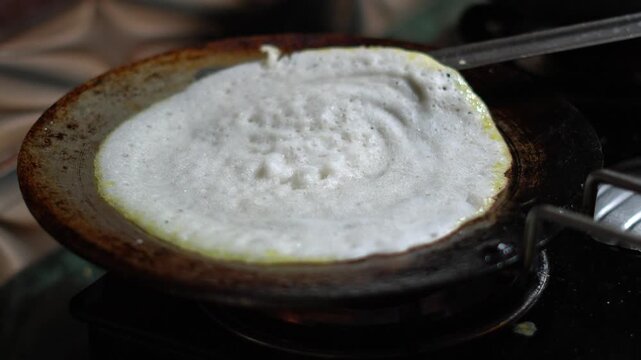 Flipping a Crispy South Indian Dosa Crepe on Hot Cast Iron Tawa Pan. Cooking Traditional Indian Dosa Pancake on Gas Stove Top in Kitchen.