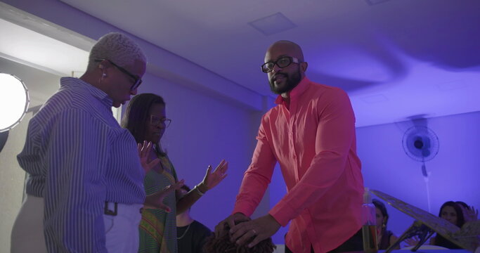 Man in bright shirt blesses kneeling boy during church service while preacher and woman look on, spiritual moment of faith and anointing