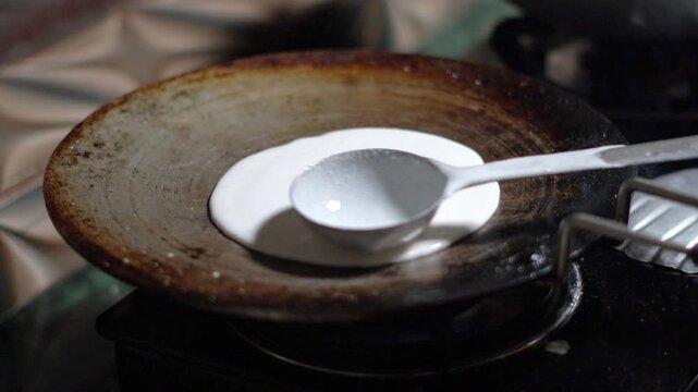 Pouring White Rice Batter with Ladle onto Hot Cast Iron Tawa for Dosa. Making Traditional South Indian Food on Gas Stove Top Close Up. South Indian Food In Indian Kitchen.