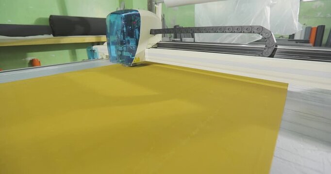 CNC Plotter. Industrial CNC Cutter Processing Technical Fabric. Digital cutting system (automatic cutting plotter) in operation. The cutting head moves along the gantry and cuts a yellow fabric