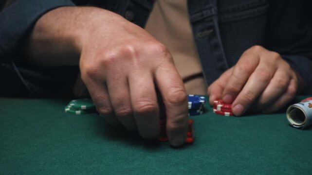 Male player craps with hands visible stacks colorful poker chips and rolls dice on a green felt table, creating a lively atmosphere in a casual gaming setting with visible game elements