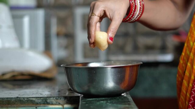 Indian Woman Dropping Soft Rasgulla Sweet into a Stainless Steel Bowl. Traditional Indian Sweet Preparation with Woman Handling Homemade Rasgulla.
