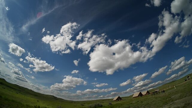 Fish-eye timelapse of white summer cumulus clouds drifting above a prairie park with camping tents
